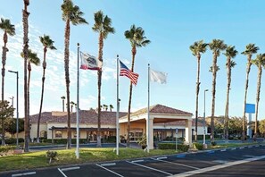 Un hotel con techo de tejas, palmeras y varias banderas, incluyendo la bandera estadounidense.