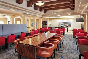 A spacious dining area with multiple tables and red chairs, a kitchen in the background, and a modern ceiling design.