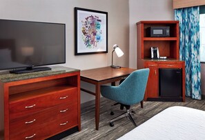 Habitación de hotel con televisor, escritorio, silla, microondas, cafetera y cama.