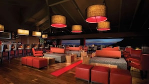 A spacious lounge area with red seating, a red carpet, and large woven lamps.