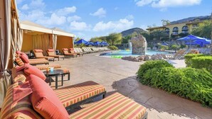 A poolside area with lounge chairs and umbrellas, a small waterfall feature, and a pool.