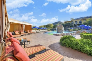 A poolside area with lounge chairs and umbrellas, a small waterfall feature, and a pool.