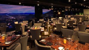 A restaurant with multiple tables set for dining, featuring a scenic cityscape view through large windows.