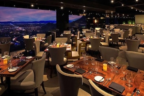 A restaurant with multiple tables set for dining, featuring a scenic cityscape view through large windows.