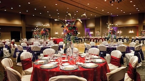 A banquet hall with round tables set for a formal event, featuring red tablecloths and white chairs with red sashes.