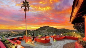 An outdoor patio area with red planters, a palm tree, and a mountainous backdrop during sunset.
