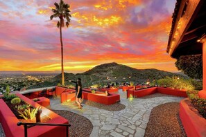 An outdoor patio area with red planters, a palm tree, and a mountainous backdrop during sunset.
