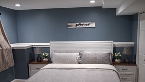 Een slaapkamer met een bed, nachtkastjes, een kunstwerk aan de muur en een plafondlamp.
