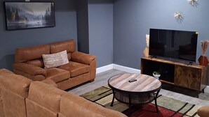 Een woonkamer met een bank, een salontafel, een televisie op een houten dressoir, en een schilderij aan de muur.