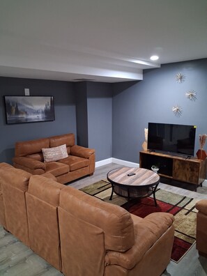 Ein Wohnzimmer mit Sofa, Couchtisch, Fernseher auf Holzfuß und einem Gemälde an der Wand.