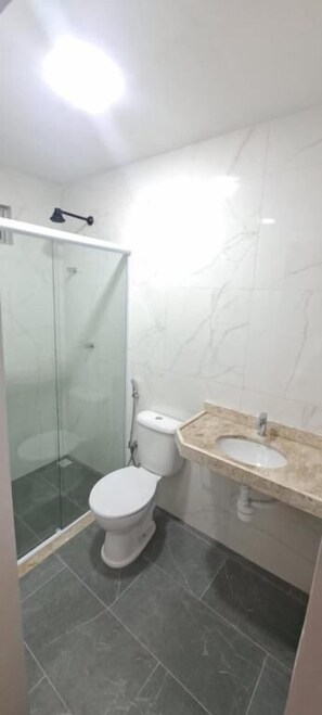 Un bany amb vàter, box de dutxa de vidre i un lavabo amb taulell de marbre.
