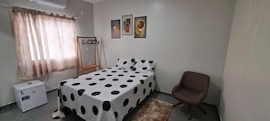 Een slaapkamer met een bed, een stoel, een verwarming en een raam met gordijnen.