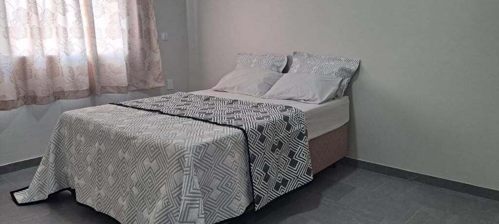 Een bed met beddengoed met patroon, een nachtkastje en een raam met gordijnen.