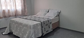Un llit amb roba de llit estampada, una taula de nit i una finestra amb cortines.