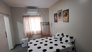 Quarto com cama, guarda-roupa, mesa pequena, cadeira e janela com cortinas.