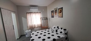 Een slaapkamer met een bed, een kledingkast, een klein tafeltje, een stoel en een raam met gordijnen.