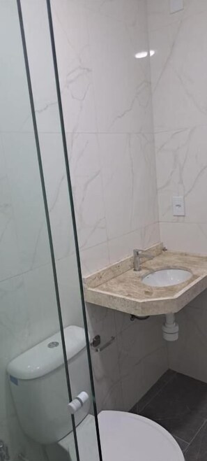 A bathroom with a glass partition, a toilet, a sink, and a marble-patterned wall. - HOSPEDARIA LENÇÓIS  (Barreirinhas)