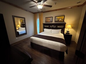 A hotel room with a bed, a ceiling fan, a nightstand with a lamp, and artwork on the walls. - 4th July Family Vacation 2-bedroom Resort Cabin with Mountain view & Water Park (Gatlinburg)