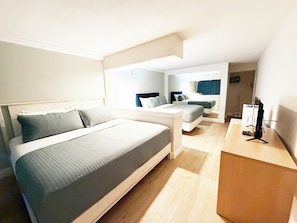 Quarto de hotel moderno com uma cama grande, uma cama menor, uma escrivaninha e uma televisão.