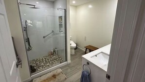 Ein Badezimmer mit einer gläsernen Duschkabine, einem weißen Waschbecken und einem kleinen Holzschemel.