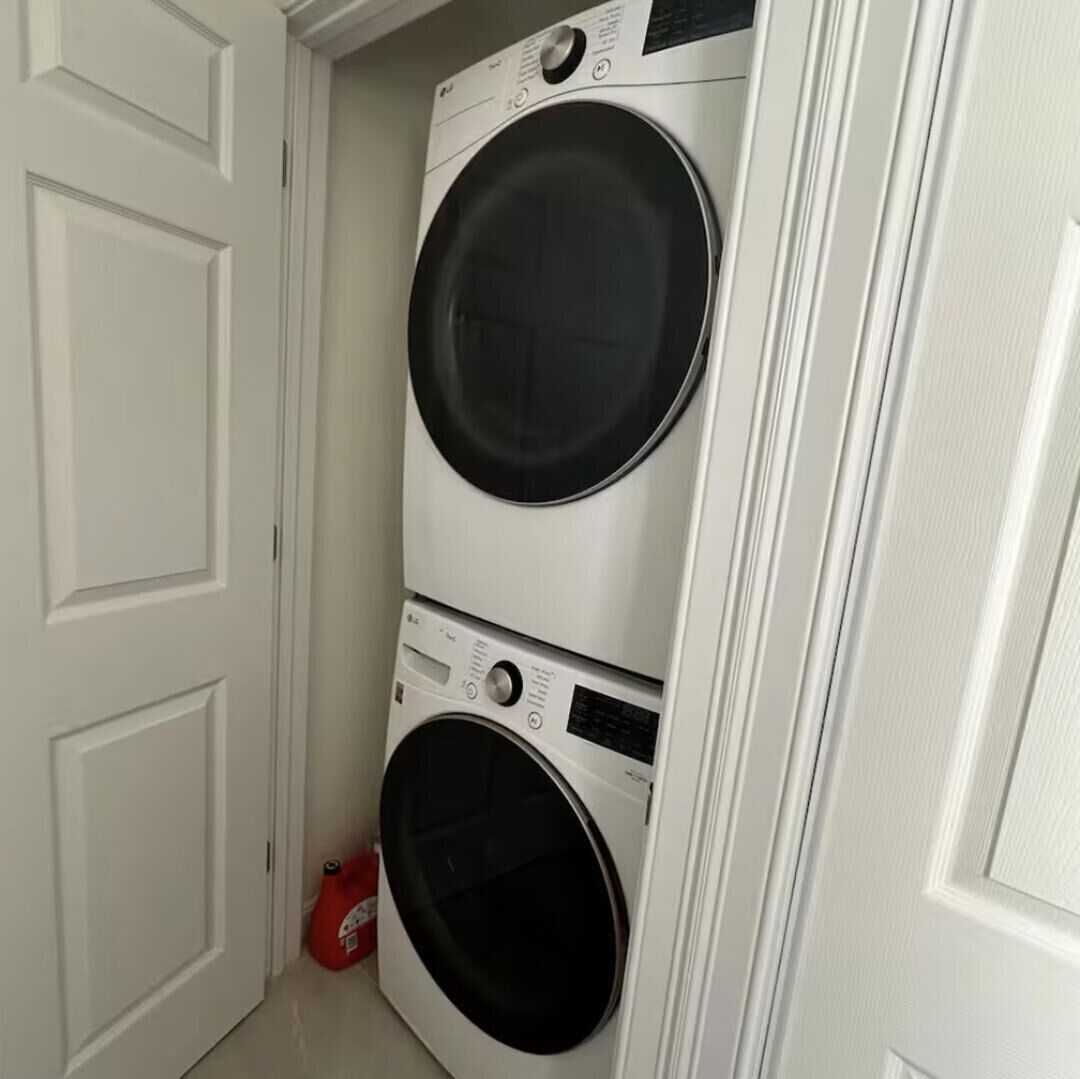 Une buanderie avec deux machines à laver à chargement frontal superposées et une bouteille de lessive rouge posée sur le sol.