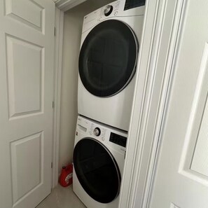 A laundry room with two stacked front-loading washing machines and a red detergent bottle on the floor.