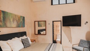 A hotel room with a large bed, a flat-screen TV mounted on the wall, a grey armchair, and a bathroom with a toilet and sink. - Charming Boutique Hotel Suite in the Heart of Merida (Mérida)