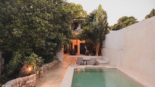 A pool area with a stone wall, a patio with chairs, and a building in the background. - Charming Boutique Hotel Suite in the Heart of Merida (Mérida)