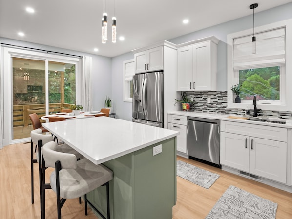 A modern kitchen with white cabinets, stainless steel appliances, and a large island with bar stools. - Airy & Stylish New Build, 4 Bedrooms, 3.5 Bathrooms, Central to all of Asheville (Asheville)