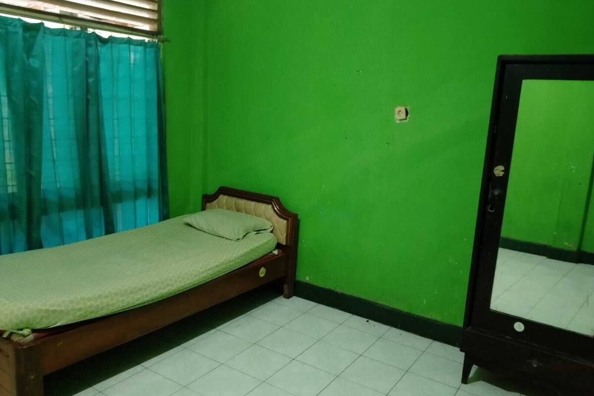 Una habitación pequeña con una cama individual, un espejo y una pared verde.