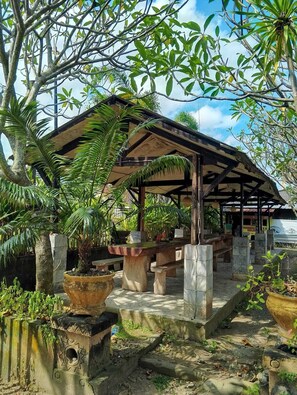 A covered outdoor seating area with stone benches and planters, surrounded by trees and greenery. - Hotel Paradiso Mataram (Mataram)