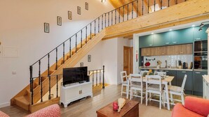 A spacious living area with a wooden staircase, a dining table with chairs, a TV on a cabinet, and a kitchen in the background. - Casa do Bocage, By Home Match (Setúbal)