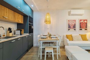 Eine moderne Küche mit dunklen Schränken, einem Esstisch für vier Personen und einem weißen Sofa mit gelben Kissen.