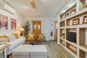 Ein Wohnzimmer mit einer Couch, Sesseln, einem Fernseher und einem Bücherregal.