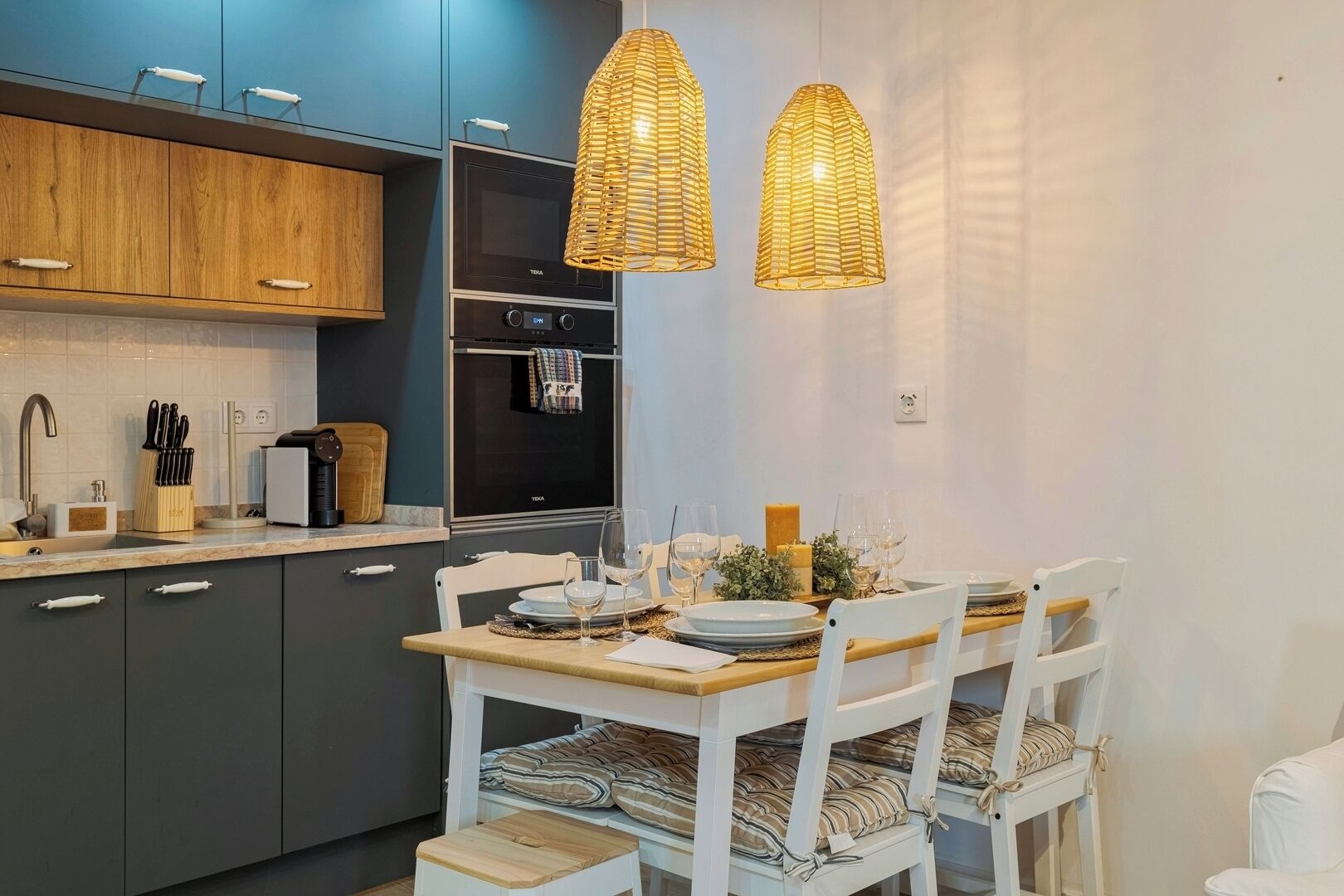 Eine moderne Küche mit dunklen Schränken, einem eingebauten Backofen und einem Essbereich mit weißen Stühlen und einem Holztisch.