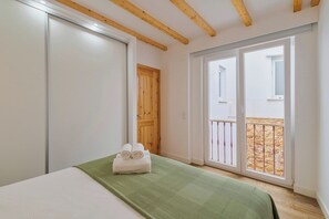 A bedroom with a bed, a green bedspread, a wooden door, and a balcony with a stone wall. - Casa do Bocage, By Home Match (Setúbal)