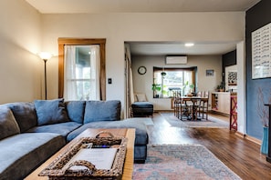 Ein Wohnzimmer mit einer Couch, einem Couchtisch mit Tablett, einem Essbereich mit Tisch und Stühlen und einer Küche im Hintergrund.