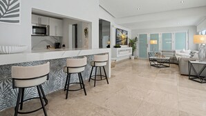 Eine moderne Küche mit Barbereich, einer Sitzecke inklusive Sofa und Couchtisch sowie einem großen Fenster.