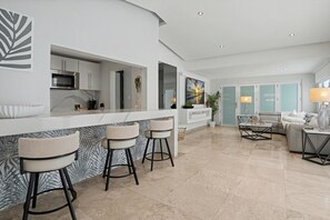 A modern kitchen with a bar area, a seating area with a sofa and coffee table, and a large window. - Venus Oasis - Pool, Game Room & Full Solar Backup - Steps to the Beach (Carolina)