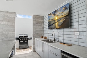 A modern kitchen with a built-in grill, a large window, and a tiled backsplash. - Venus Oasis - Pool, Game Room & Full Solar Backup - Steps to the Beach (Carolina)