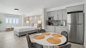 Ein modernes Schlafzimmer mit einem großen Bett, einem Esstisch mit Platzsets, einer Küche mit Edelstahlgeräten und Blick ins Freie.