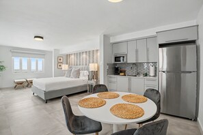 A modern bedroom with a large bed, a dining table with placemats, a kitchen with stainless steel appliances, and a view of the outdoors. - Venus Oasis - Pool, Game Room & Full Solar Backup - Steps to the Beach (Carolina)