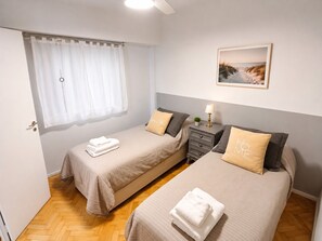 A bedroom with two beds, a window with curtains, a bedside table with a lamp, and a framed picture on the wall. - Apartment in Recoleta, close to all tourist attractions. (Buenos Aires)