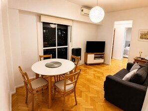 A living room with a round table, two wooden chairs, a sofa, a television, and a large window with a view of the city at night. - Apartment in Recoleta, close to all tourist attractions. (Buenos Aires)