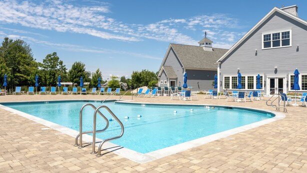 A swimming pool with blue chairs and umbrellas, a building with a gabled roof, and a clear sky.