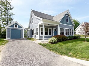 Een tweelaags huis met een overdekte veranda, een garage en een verzorgd gazon.