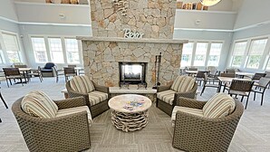 A spacious lounge area with wicker furniture, a stone fireplace, and large windows.