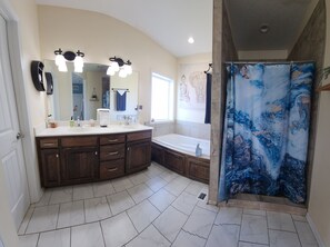 A bathroom with a double sink vanity, a bathtub, a shower curtain, and a large mirror. - Group Stays, Sleep 8-10, Near KC, Pet Friendly, 3 acres (Odessa)