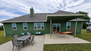 Een groene woning met terras, een tafel met stoelen en een hangmat.
