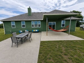 A green house with a patio, a table with chairs, and a hammock. - Group Stays, Sleep 8-10, Near KC, Pet Friendly, 3 acres (Odessa)